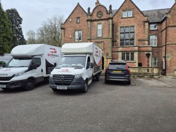 Two Apex Removals vans parked outside a large brick manor house during a multi-van relocation