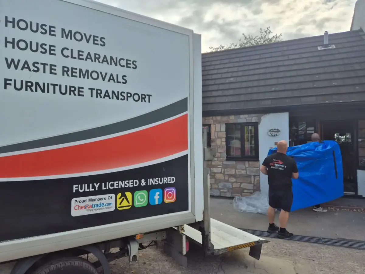 Apex Removals truck outside a stone cottage with crew handling a wrapped item